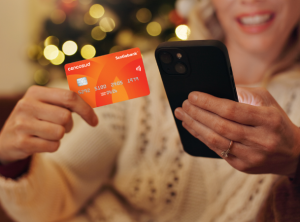 Mujer con tarjeta Cencosud mirando su celular para comprar regalos para Navidad Tarjeta Cencosud frente al árbol navideño