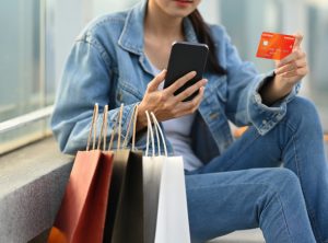 Mujer joven sonriendo mientras sostiene varias bolsas de colores y una tarjeta de crédito negra para sus compras de semana santa 2026